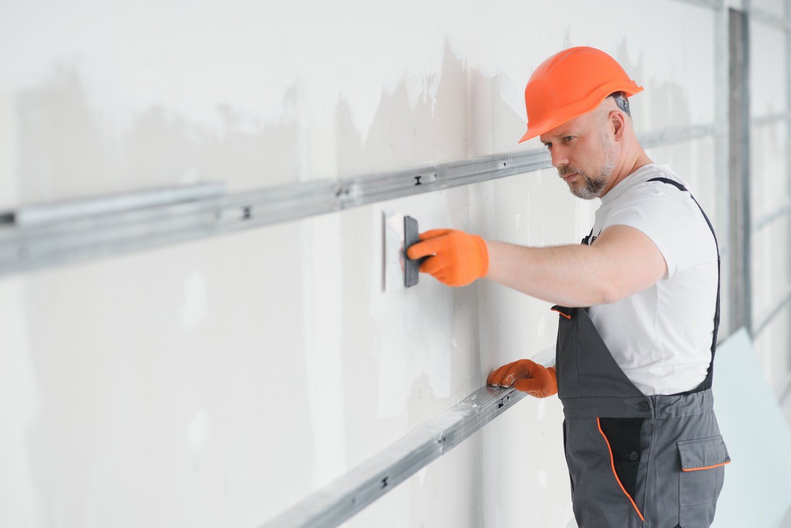 man drywall worker using trowel for plasterer putting stucco on plasterboard white wall.